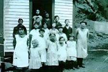 01 School kids c. 1929. Joe Lockyer is standing by the school on the left Lilly Lockyer is ahead of him in the front row, next to her is Mae Hamilton Lockyer, the taller girl is unknown, next to her is Susie Green, the little one is Violet Williams Lockyer, Annie Lockyer and Lola Williams Lockyer. The second row is Bertha Williams Hapgood and her sister Mabel, Rose Hamilton Williams. The rest remain unknown. Credit: Joe Lockyer